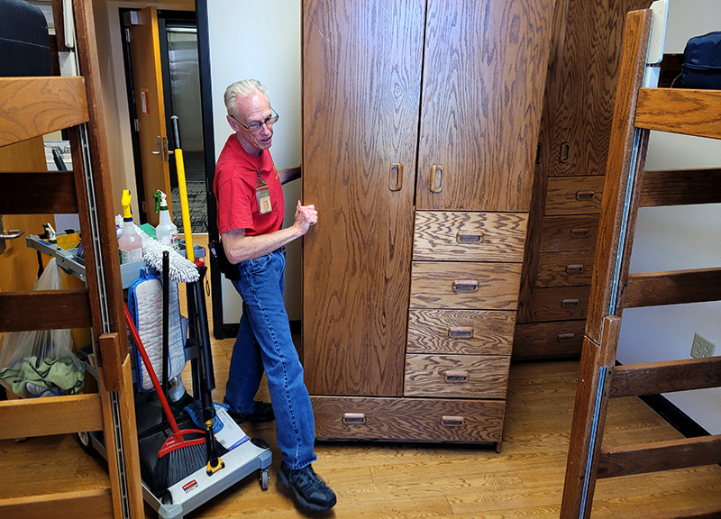 Man in T-shirt and jeans moves wooden wardrobe in dorm room