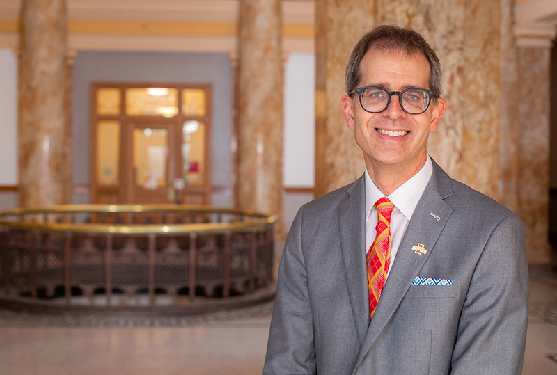 Man with glasses in gray suit and plaid tie in building rotunda