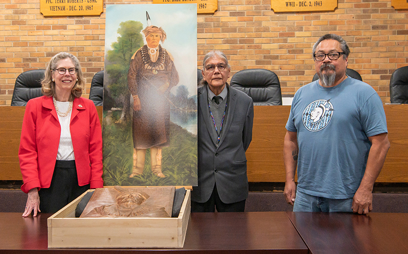 White woman and two Native American men flank painting and boxed