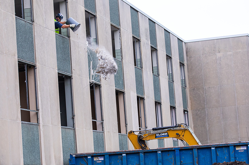 Worker tosses bucket of materials out building window into dumps