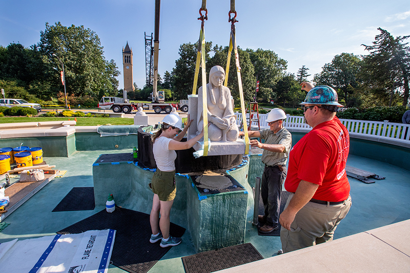 woman and man guide suspended limestone sculpture into place