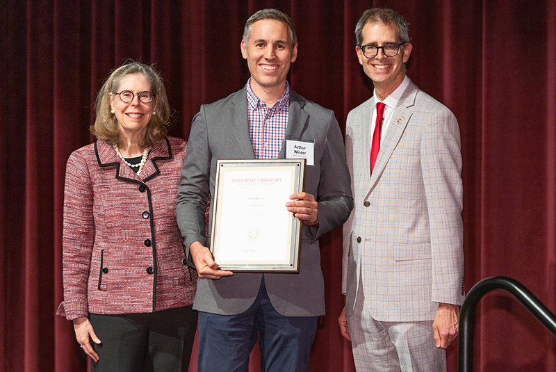 Man with framed award, flanked by male and female leaders