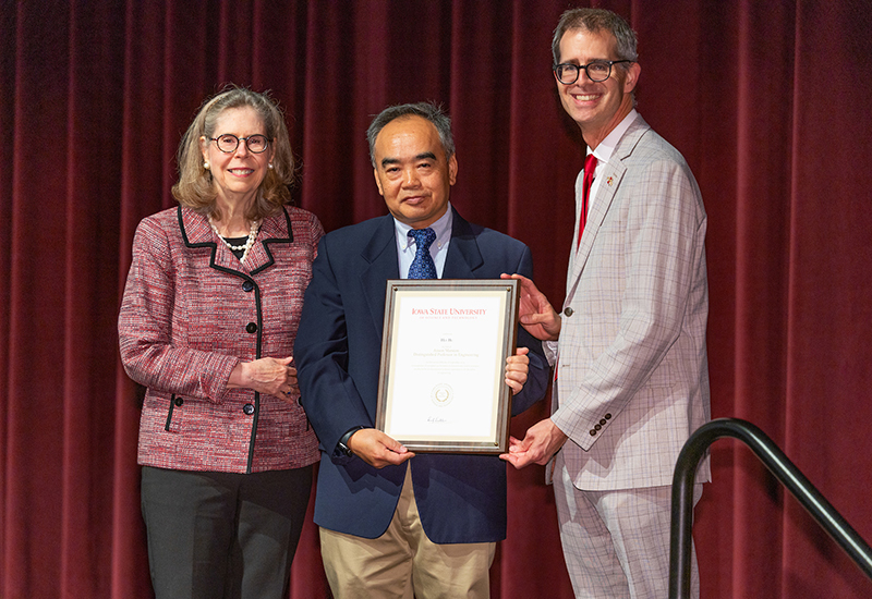 Asian man holds framed award, flanked by male and female leaders