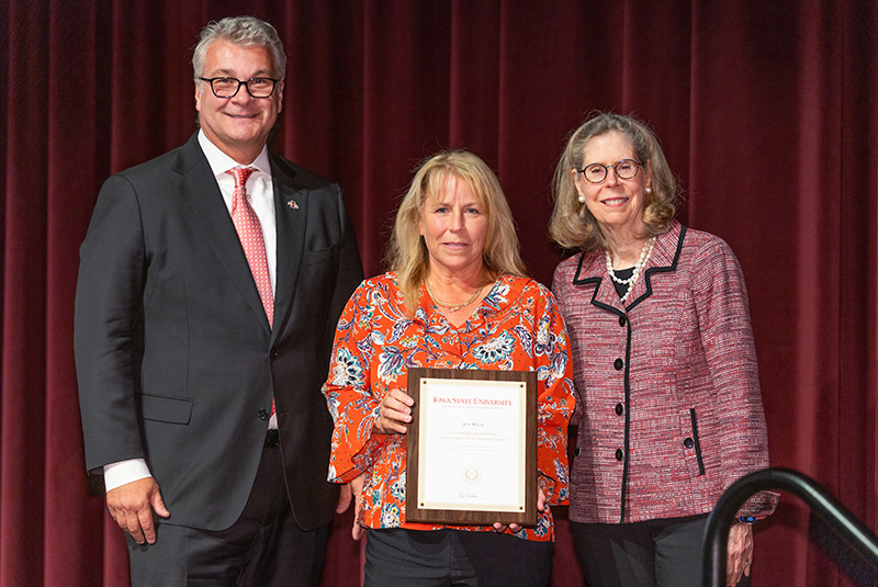 Woman with framed award, flanked by male and female leaders