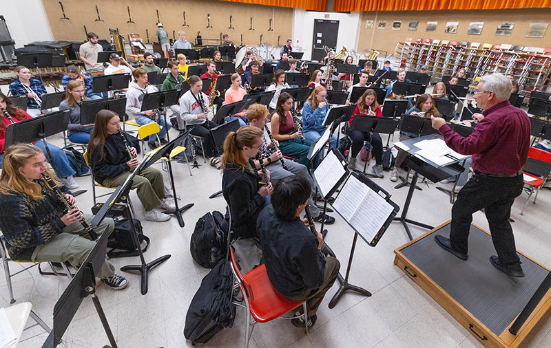 Male band director directs seated student musicians