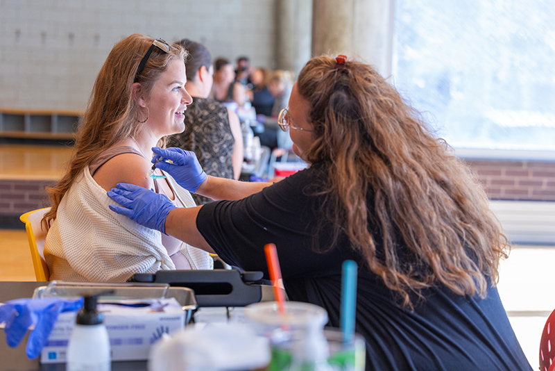 Female nurse in purple gloves administers vaccine to female empl