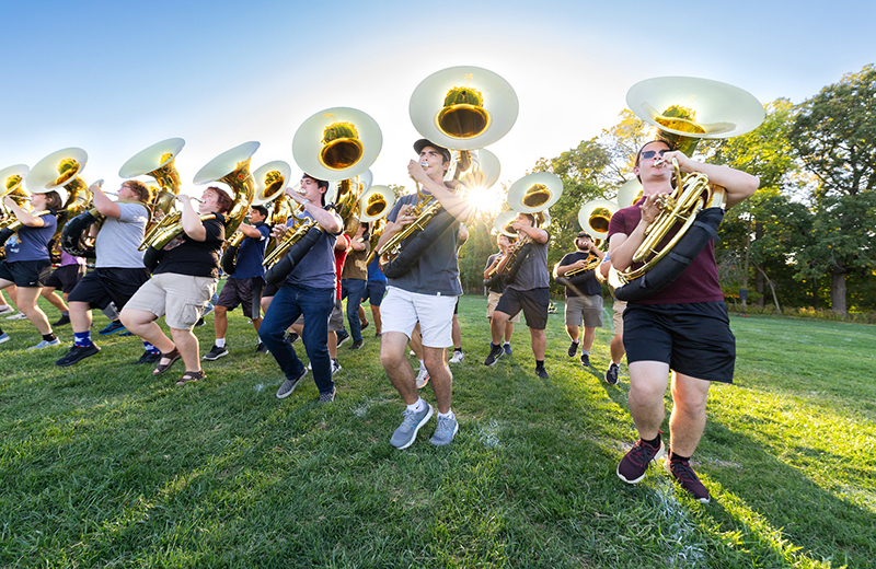 Male sousaphone players march and play on practice field