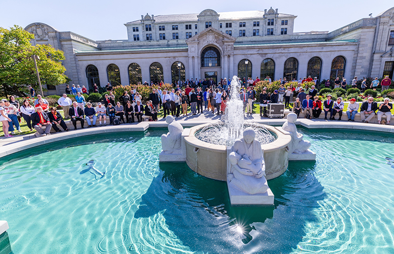 A crowd gathers around a fountain sculpture and water basin