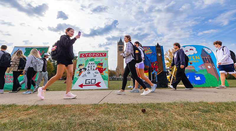 Students pass by 10-foot square framed posters along sidewalk