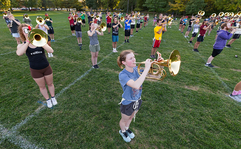 male and female students in shorts and T-shirts playing brass ho