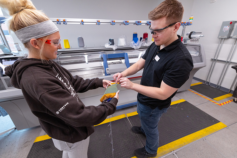 Female student in brown hoodie and male wearing goggles discuss 