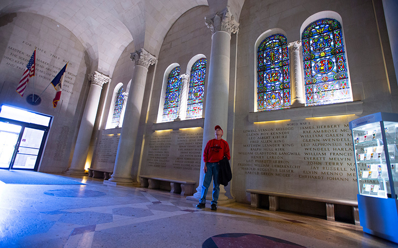 Man stands in limestone foyer with stained glass and names carve