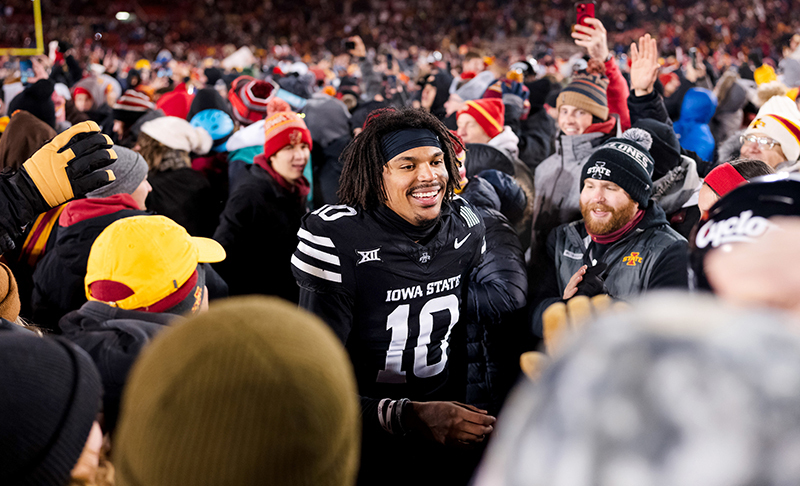 Football player in black uniform is surrounded by fans on field