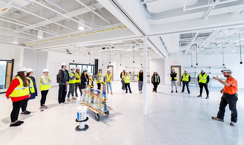 Students in hard hats stand in semi circle while project manager