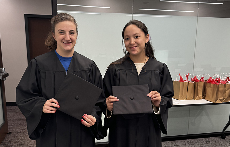 Two female students pose in black graduation gowns