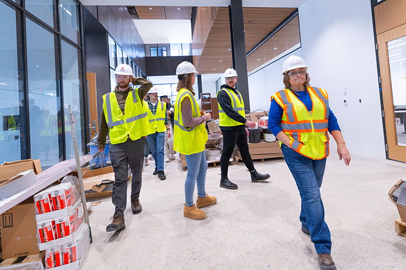 Students and woman project manager walk in hallway cluttered wit