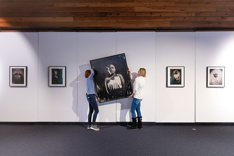 Two women hang large framed photograph on wall